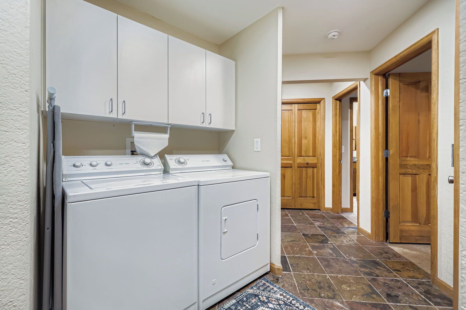 A laundry area with a washer and dryer, wooden cabinets, and a tiled floor.