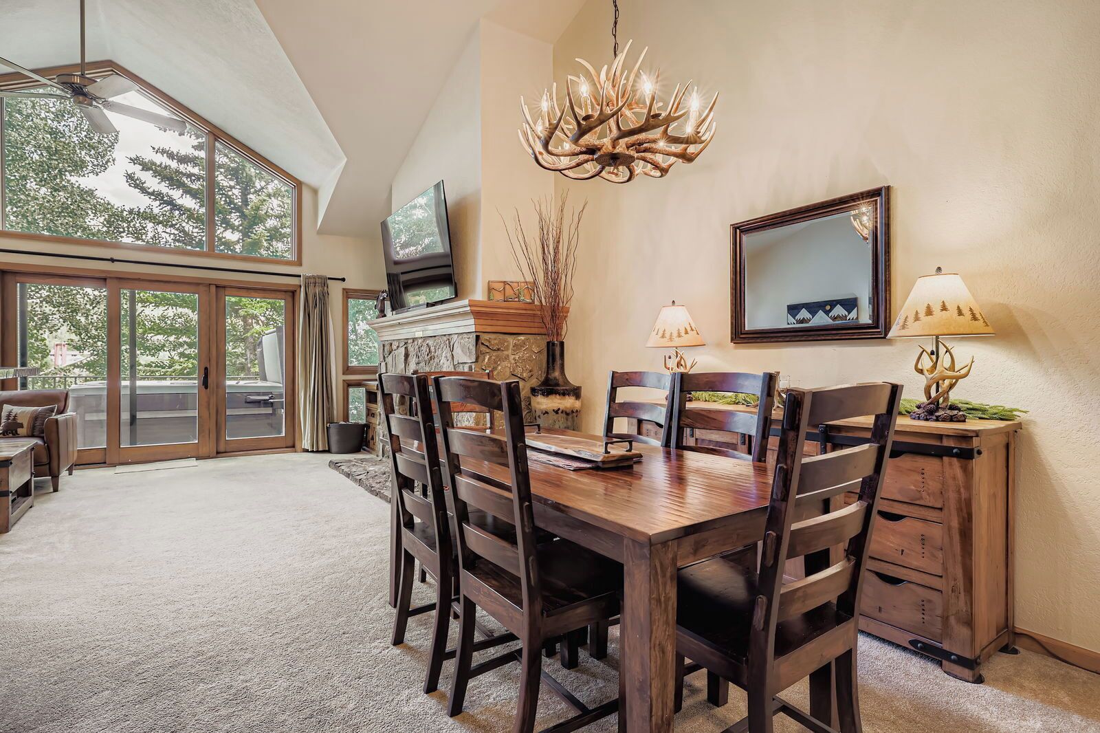 A dining area with a large wooden table, chairs, a chandelier, a television, and a fireplace.