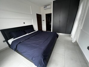 Relax in a serene bedroom with a large bed, minimalist decor, and a convenient air conditioning unit.