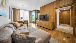 Een moderne woonkamer met een bank, televisie, wandpaneel van hout en een eethoek.