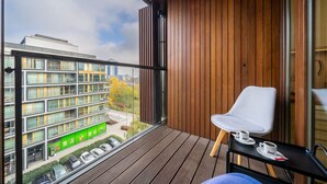 Een balkon met een houten vloer, een witte stoel en een klein tafeltje met kopjes.