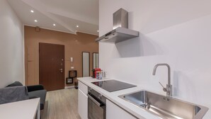 A modern kitchen with a stainless steel sink, a built-in oven, and a range hood. There is a dining area with a white table and a grey sofa. - CORSO GARIBALDI 64 - LIVING MILAN (Milan)