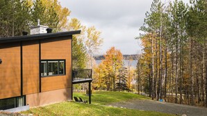 Una casa moderna amb un balcó que dona a una zona boscosa i una extensió d'aigua.