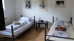 A room with two single beds, a small table, and a wall-mounted shelf. - Fitters' apartment for two  (Schleiden)