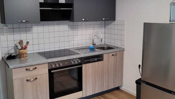 A modern kitchen with a built-in oven, dishwasher, and a stainless steel refrigerator. - Fitters' apartment for two  (Schleiden)