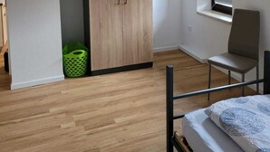 A bedroom with a bed, a chair, a wardrobe, a window, and a green basket. - Fitters' apartment for two  (Schleiden)