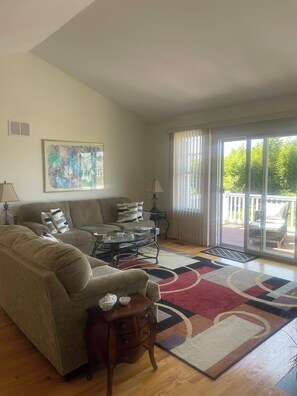 A living room with a sofa, coffee table, and a rug. There is a painting on the wall and a window with curtains.