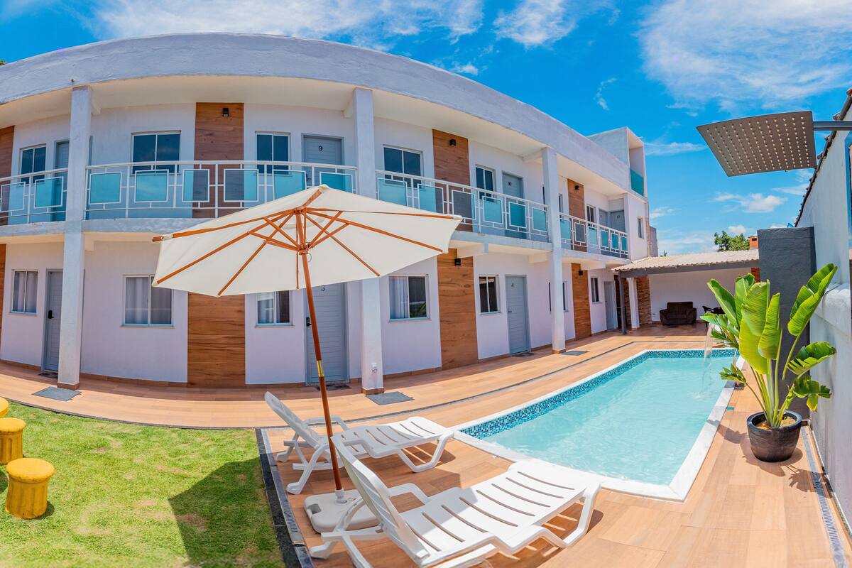 A modern multi-story building with a swimming pool, outdoor seating, and a large umbrella.