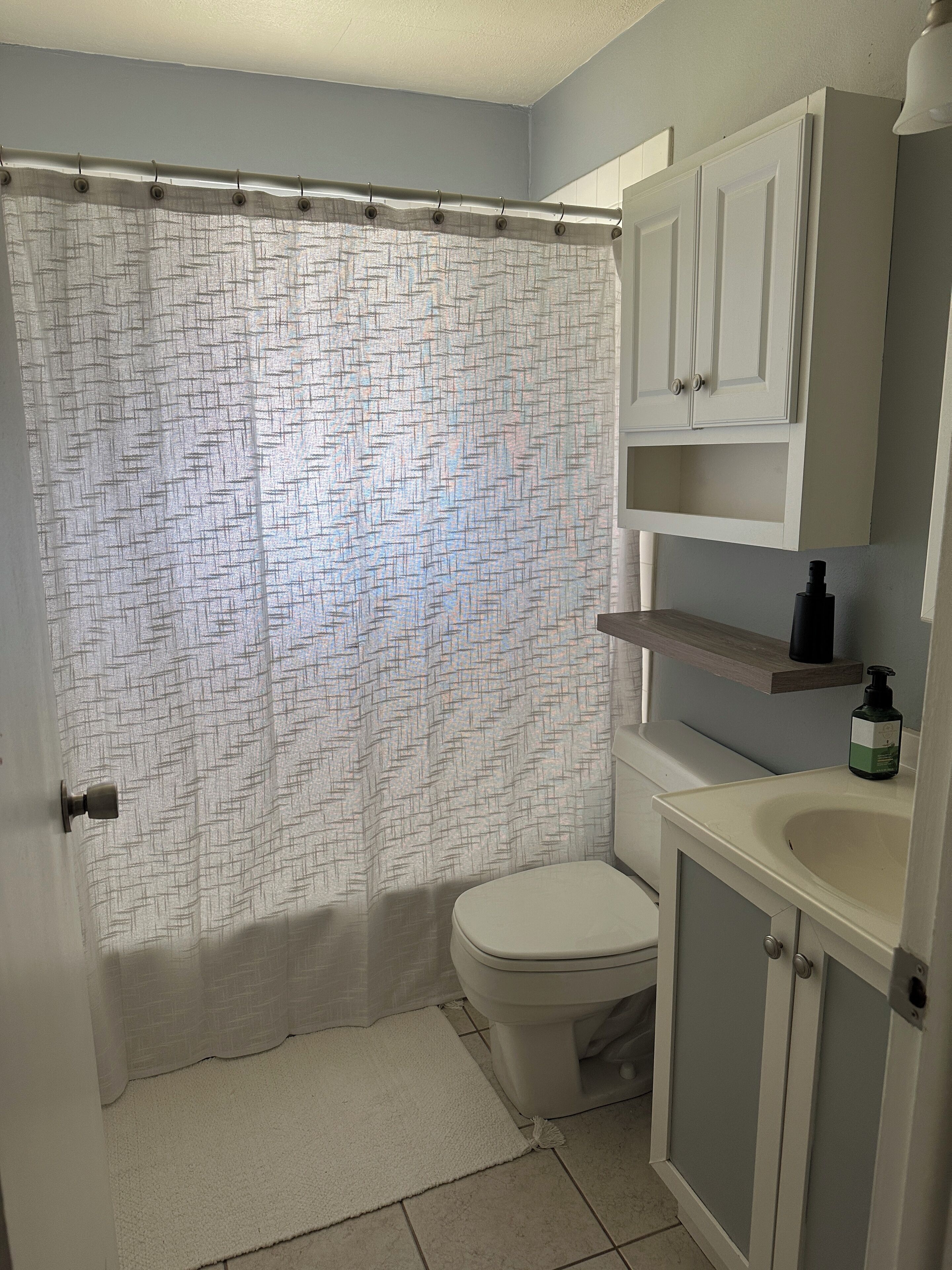 Een badkamer met douchegordijn, toilet, wastafel en kastjes.