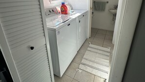 Eine kleine Küche mit Waschmaschine, Spüle und einem Fenster mit rotem Vorhang.