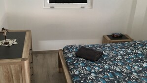 A bedroom with a bed, a small wooden desk, a nightstand, and a wall-mounted TV.