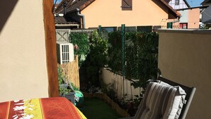 A patio with a striped chair and a cat, a small garden, and a view of neighboring houses.