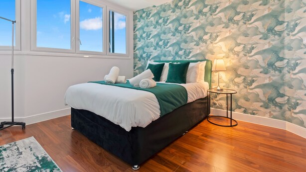 A bedroom with a bed, a nightstand, a lamp, and a window. - Emerald Suite- Bham Citycentre- Luxury-cinema Room (Birmingham)