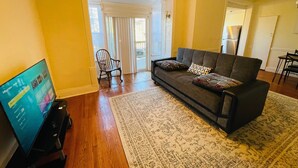 A living room with a sofa, a television, a patterned rug, and a door leading to a balcony. - Montgomery Unit1 in Elkins Park (Elkins Park)