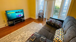 A living room with a flat-screen TV, a grey sofa, a patterned rug, and a wooden floor. - Montgomery Unit1 in Elkins Park (Elkins Park)