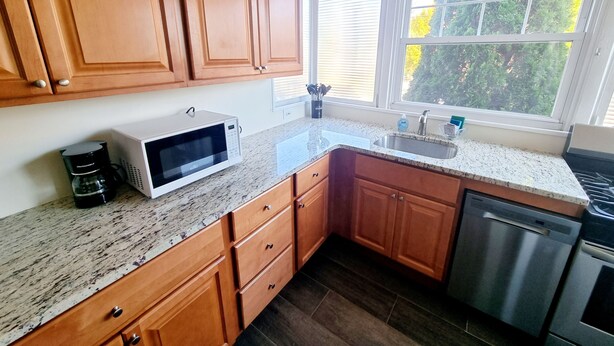 A kitchen with wooden cabinets, a microwave, a coffee maker, a sink, and a dishwasher. - Montgomery Unit1 in Elkins Park (Elkins Park)