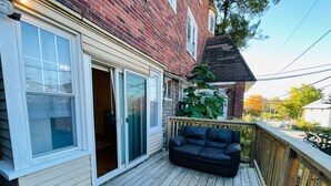 A wooden deck with a sliding glass door leading to a room, a black sofa, and a large plant. - Montgomery Unit1 in Elkins Park (Elkins Park)