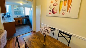 A dining area with a wooden table and chairs, a vase of flowers, and a kitchen in the background. - Montgomery Unit1 in Elkins Park (Elkins Park)