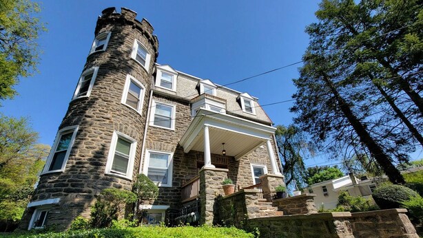 A stone castle-like house with a central tower, a porch, and a staircase leading up to the entrance. - Charming Place to Call Home (Elkins Park)