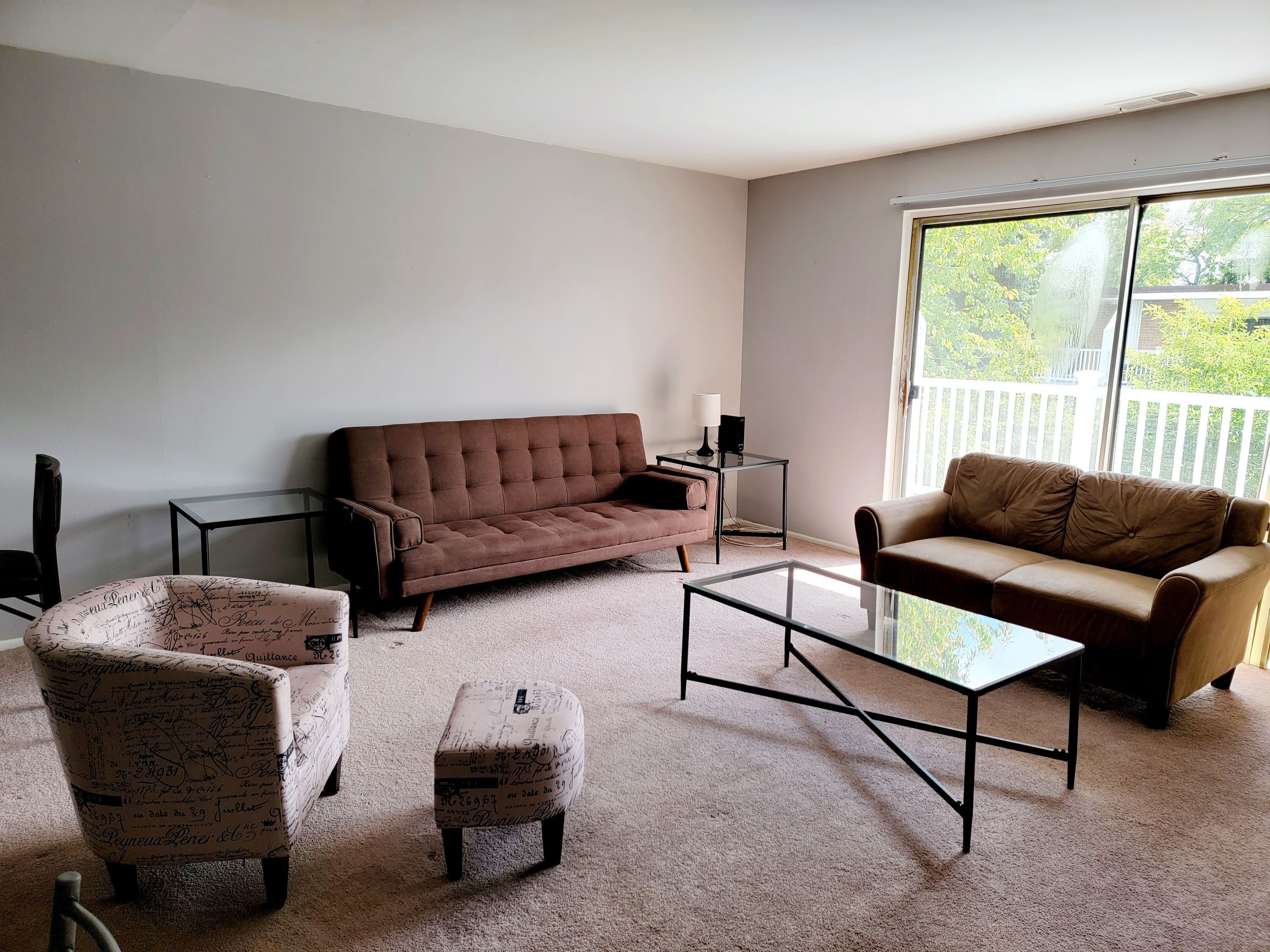 A living room with a brown sofa, a beige sofa, a patterned armchair, and a glass coffee table.