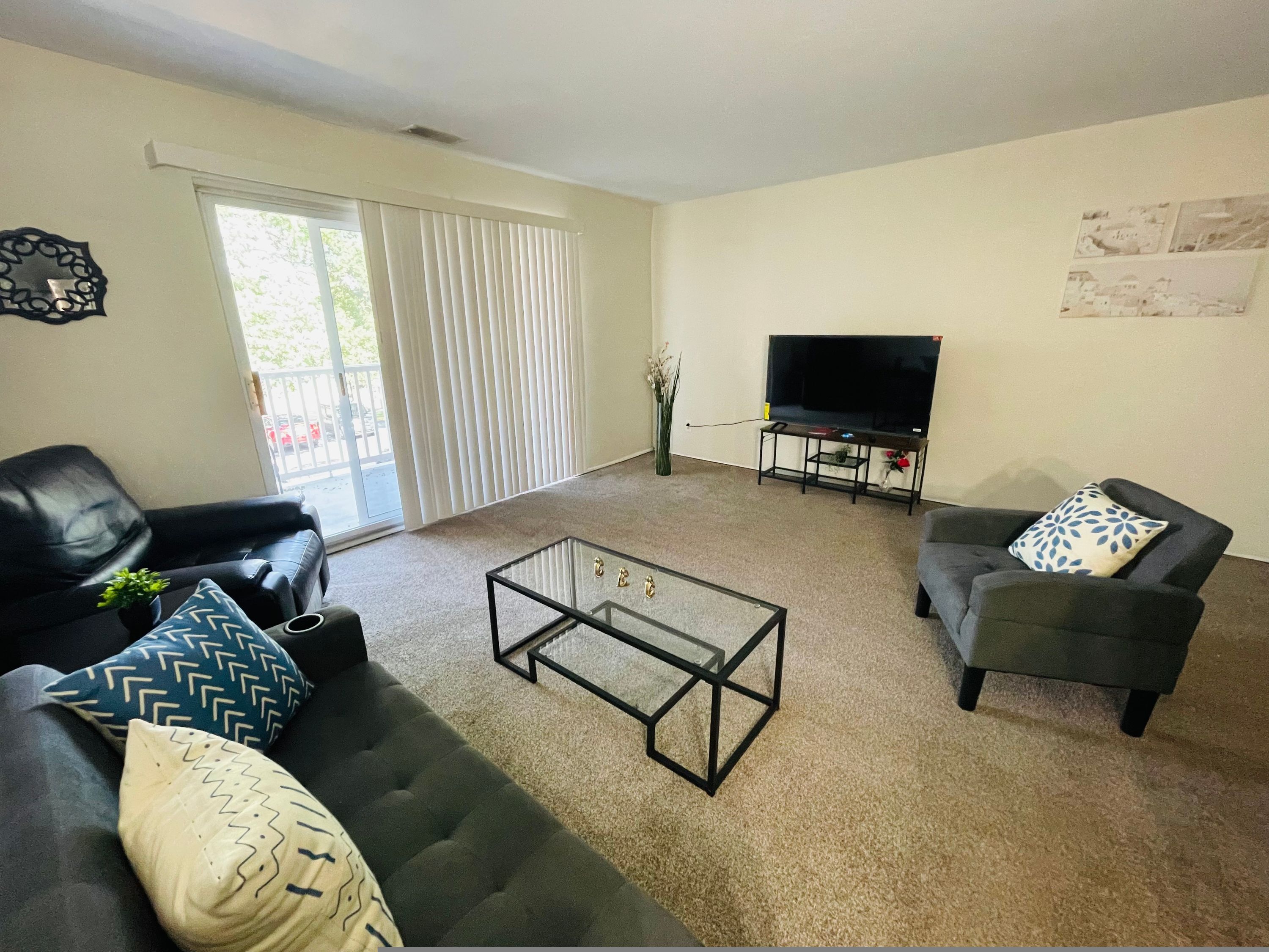 A living room with a sofa, armchair, coffee table, TV, and a sliding door.