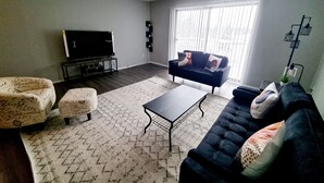 Un salon comprenant un canapé, un pouf, une table basse et un téléviseur posé sur un meuble.