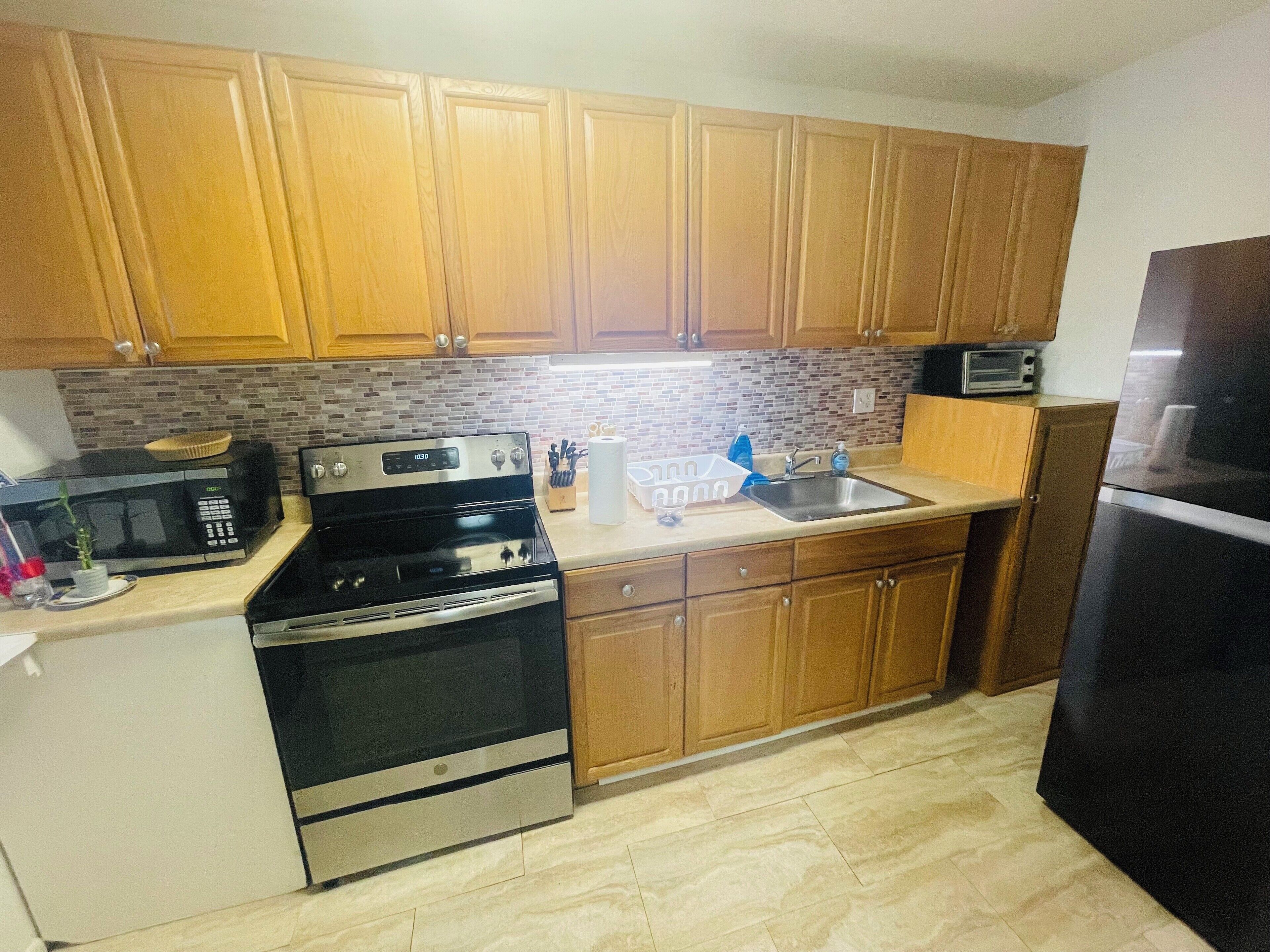 A kitchen with wooden cabinets, a stainless steel stove, a microwave, a sink, and a refrigerator.