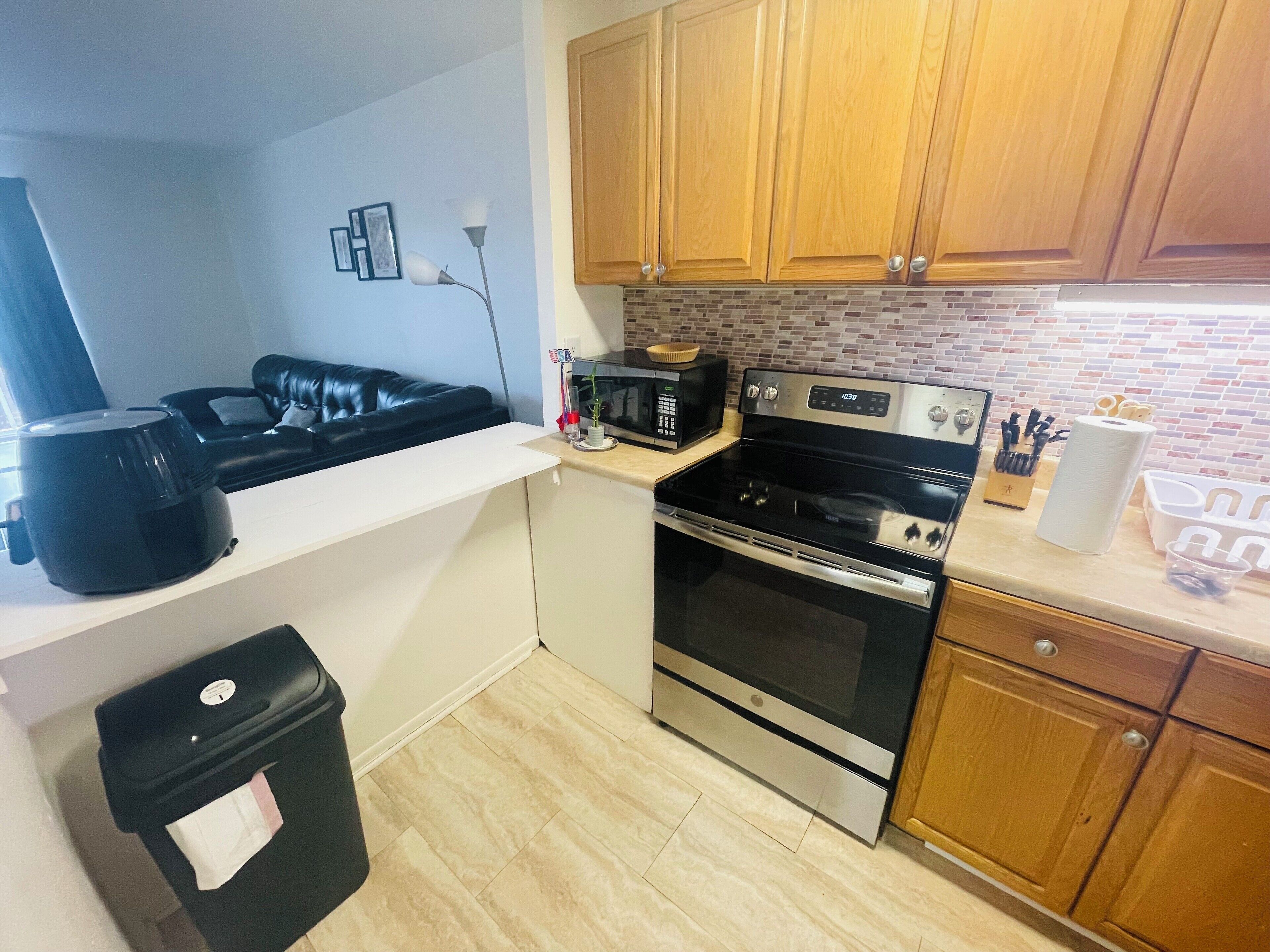 A compact kitchen with a microwave, stove, and a trash bin.