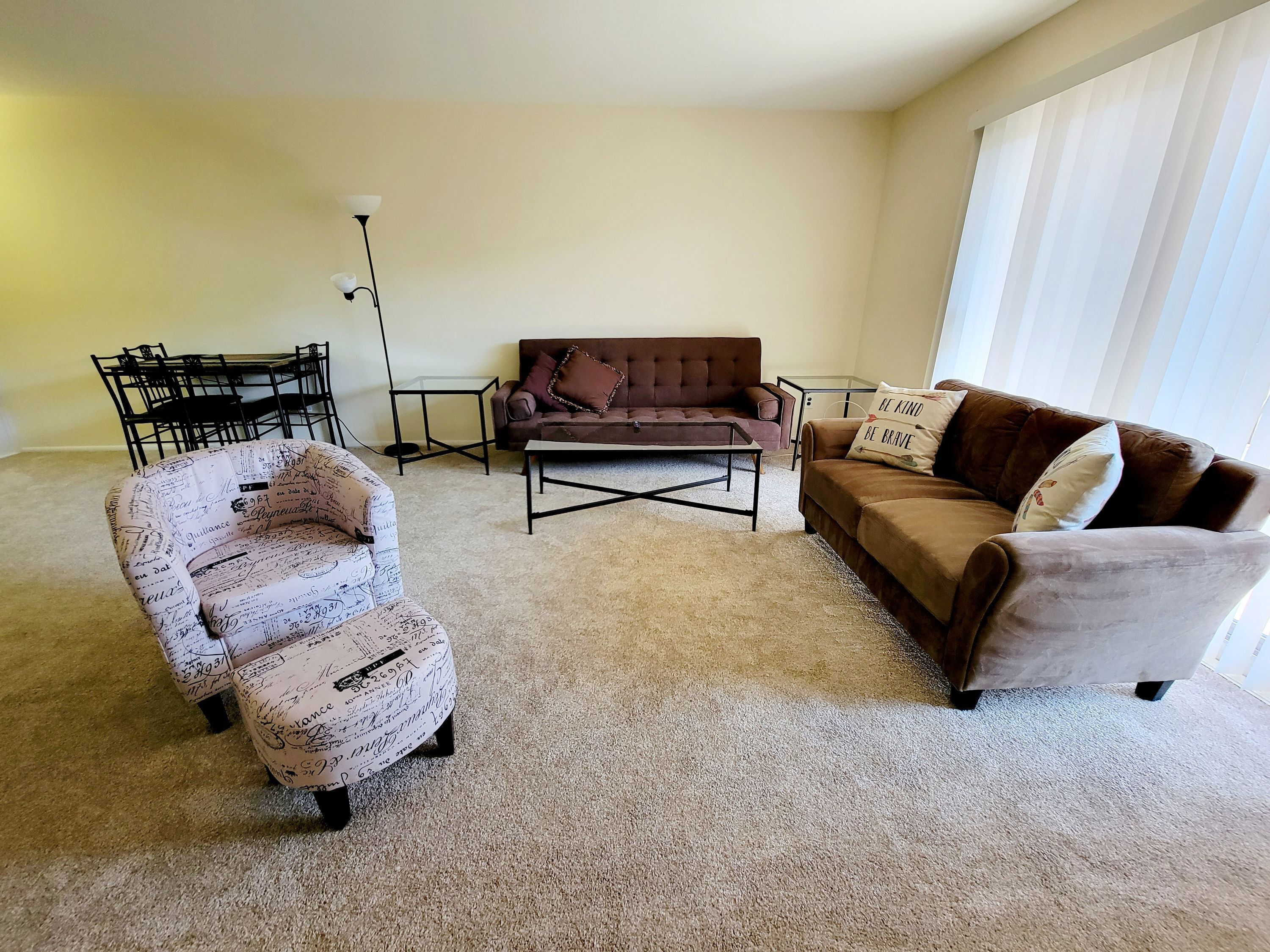 A living room with a brown sofa, a patterned armchair, a coffee table, and a floor lamp.