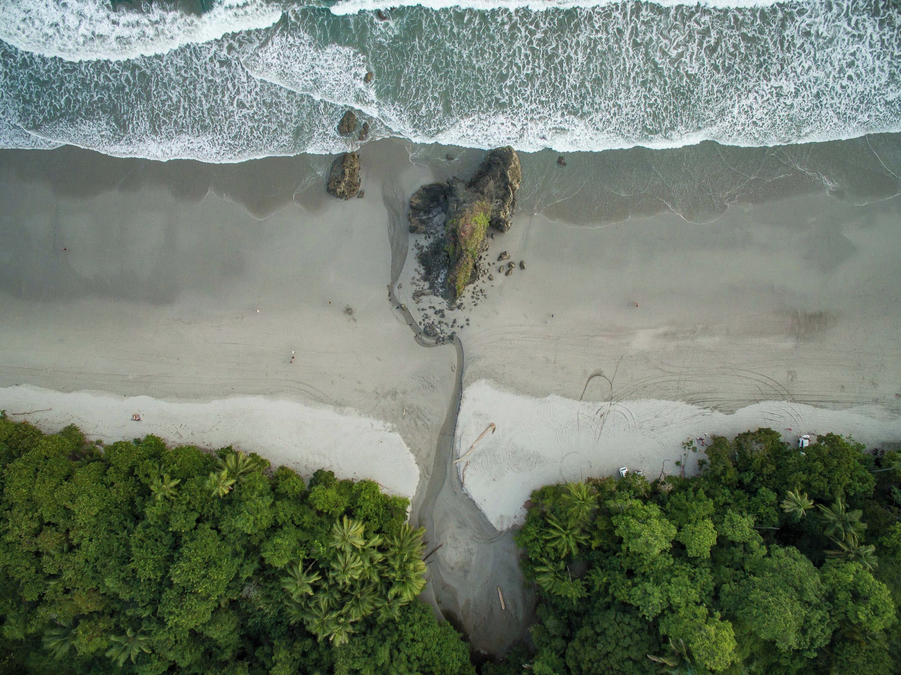 Vue aérienne d’une plage avec des affleurements rocheux et une végétation verdoyante et dense.