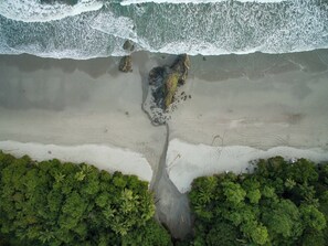 An aerial view of a beach with rocky outcrops and dense green vegetation.