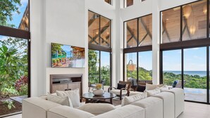 A modern living room with a large sofa, a fireplace, and a television displaying a scenic view.