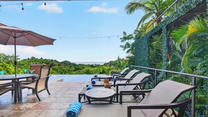 An outdoor seating area with tables and chairs, overlooking a pool and lush greenery.