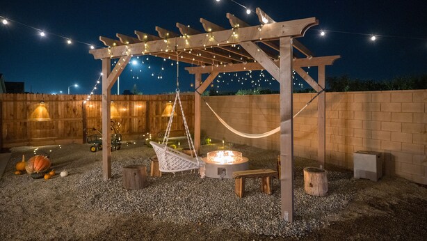 Una pérgola de madera con luces colgantes, una hamaca, un brasero y una mesita.