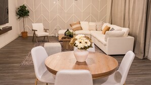 Una sala de estar moderna con una mesa de comedor redonda de madera, sillas tapizadas de blanco, un sofá blanco, un sofá beige y una araña.