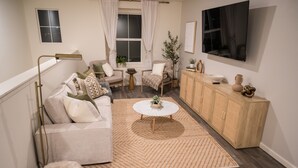 Una sala de estar moderna con sofá, sillón, mesa de centro y televisor montado en la pared.