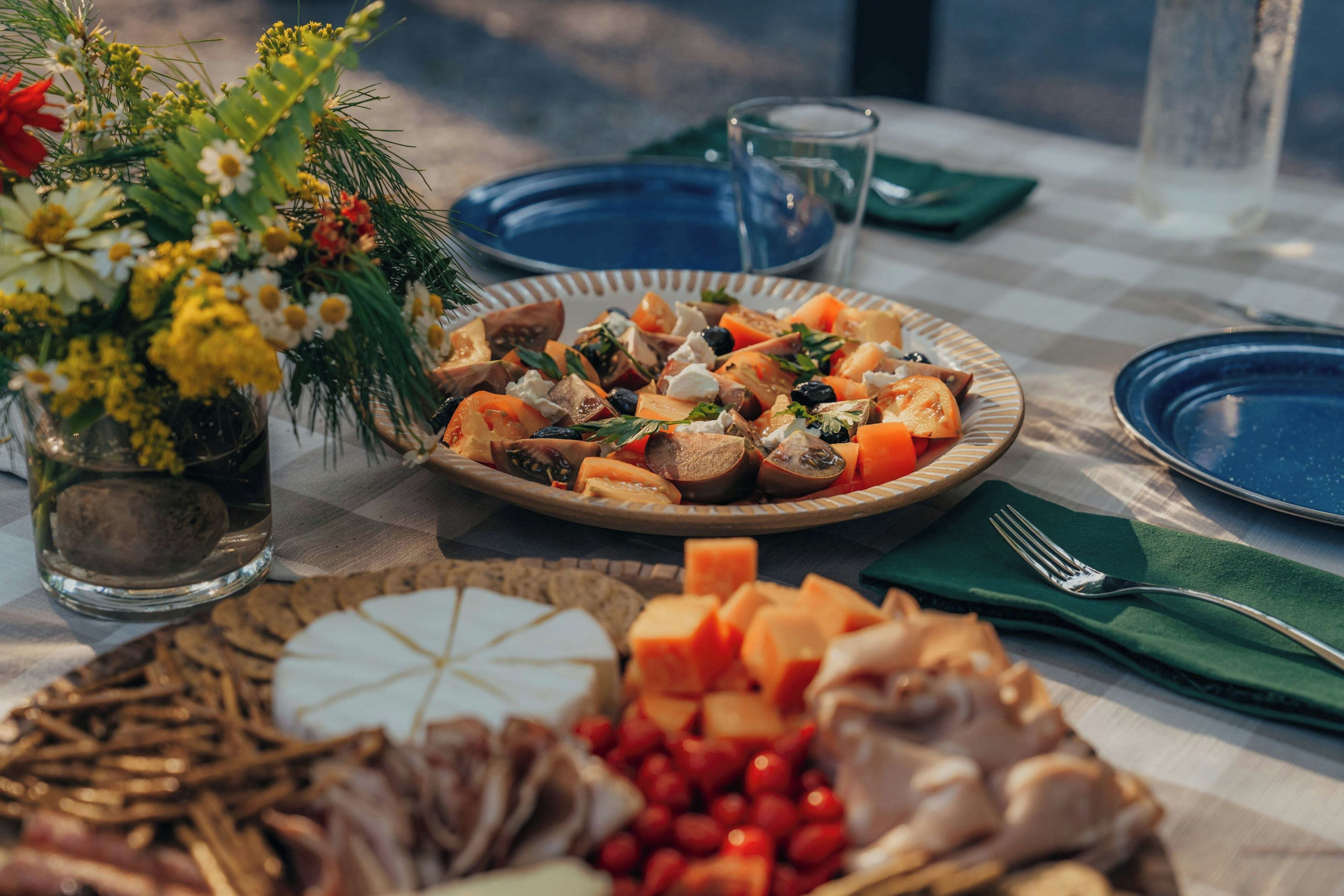 Una mesa servida con diversos alimentos, incluyendo un plato de vegetales cortados, un bol de fruta y un vaso de agua.