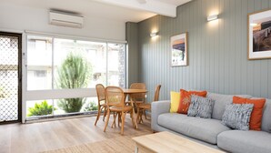 A living room with a grey sofa, wooden chairs, a coffee table, and a large window with a view of greenery and buildings.