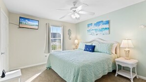 A bedroom with a bed, a ceiling fan, a TV mounted on the wall, and a window with curtains. - Colony Club H6 with Pool (Gulf Shores)