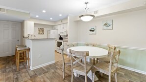A kitchen with white cabinets, a white countertop, and a hanging light fixture. There is a dining table with four chairs and a bench. - Colony Club H6 with Pool (Gulf Shores)