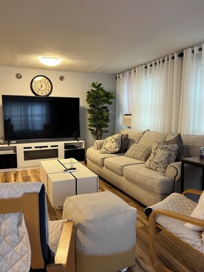 Una sala de estar con un televisor de pantalla plana, un sofá, una mesa de centro y una planta.