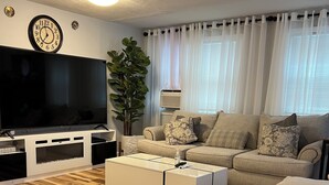 A living room with a flat-screen TV, a sofa set, a coffee table, and a wooden floor. - Sherizee Home close to beach and 3 miles to Salem's Haunted happenings (Marblehead)