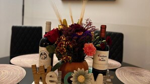 A table with a centerpiece of flowers and two bottles of wine, a 'Welcome' sign, and a modern painting on the wall. - Sherizee Home close to beach and 3 miles to Salem's Haunted happenings (Marblehead)