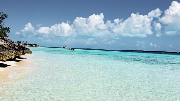 Una playa con aguas turquesas cristalinas, una costa rocosa y un barco a lo lejos.