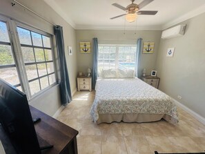 Quarto com cama, duas mesas de cabeceira, ventoinha no teto e janela com cortinas.