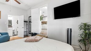 A bedroom with a bed, a TV, a ceiling fan, a potted plant, and a bathroom visible through an open door. - Near HSU, ACU & Hendrick ~ Clean ~ Charming Cottage  ~ New Discounts ~ Dogs (Abilene)