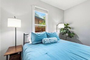 Ein Schlafzimmer mit einem Bett, zwei Nachttischlampen, einem Fenster und einem kleinen Tisch.