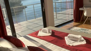 Een hotelkamer met een groot bed, rood-wit beddengoed, uitzicht op een meer en bergen, en een balkon met een leuning.