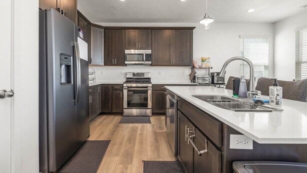 A modern kitchen with dark wood cabinets, stainless steel appliances, and a white countertop.