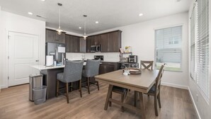 A modern kitchen with dark cabinets, a central island, and a dining area with a wooden table and chairs.